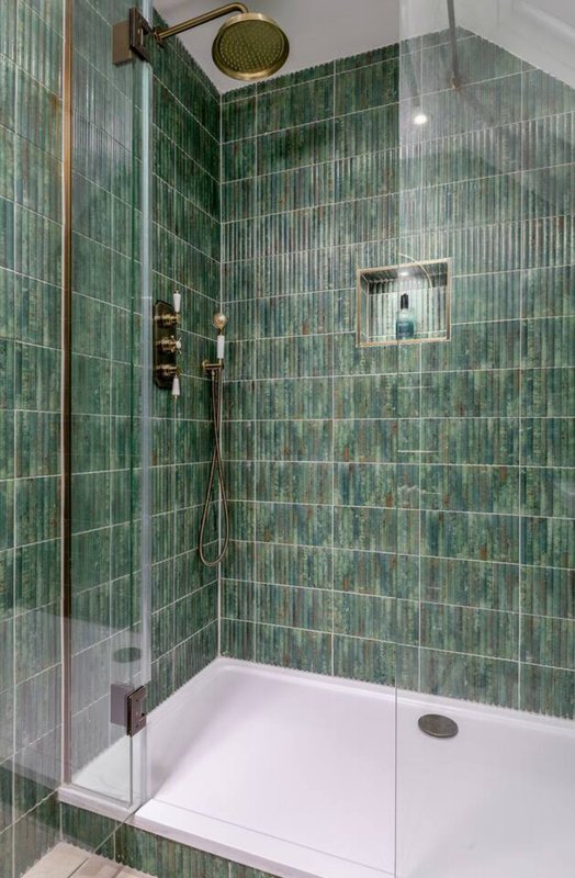 Modern bathroom shower enclosure with green tile walls and brass fixtures