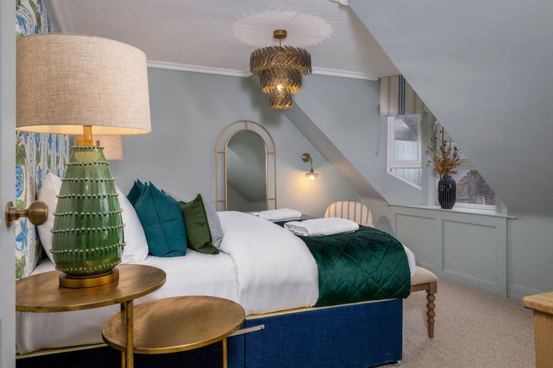 Attic bedroom with double bed, green velvet cushions, wooden furniture, and decorative lighting