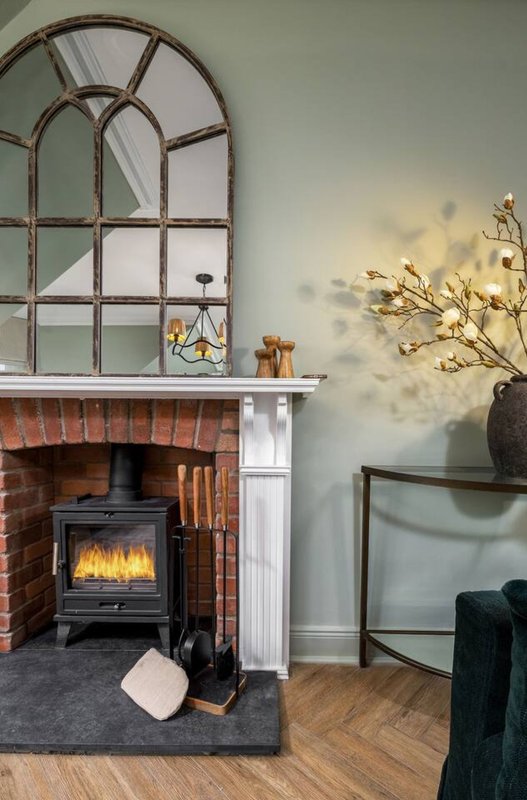 Living room with brick fireplace, black wood stove, arched mirror, dried flowers, wooden floor
