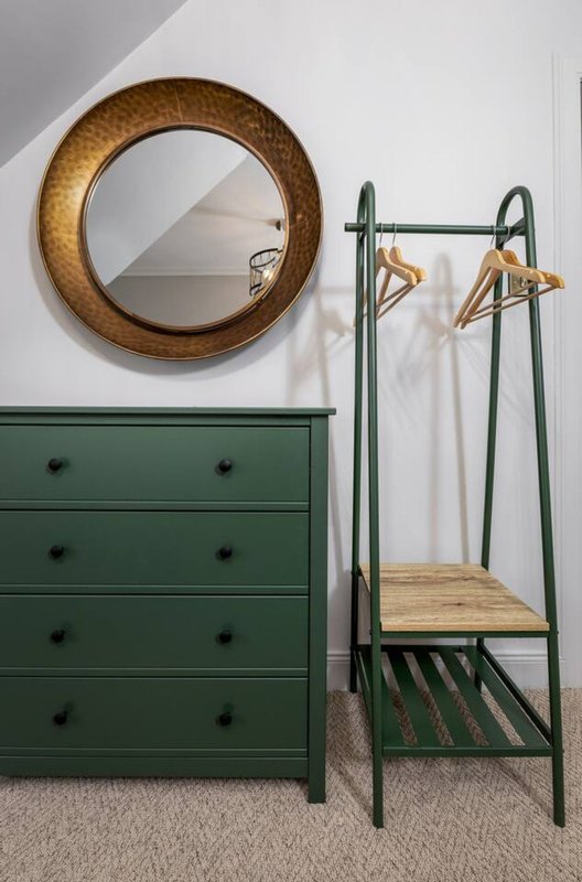Bedroom corner with green dresser, round mirror, clothing rack with hangers and white garments