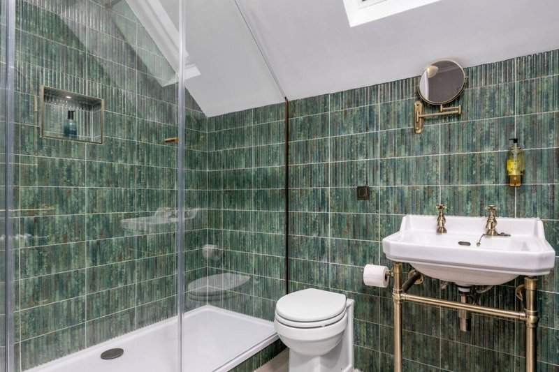 Bathroom with green tile walls, glass shower enclosure, toilet, and pedestal sink
