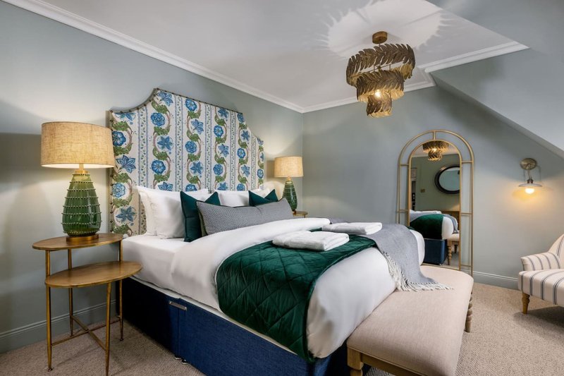Modern bedroom with blue upholstered bed, patterned headboard, gold pendant light, and ensuite visible