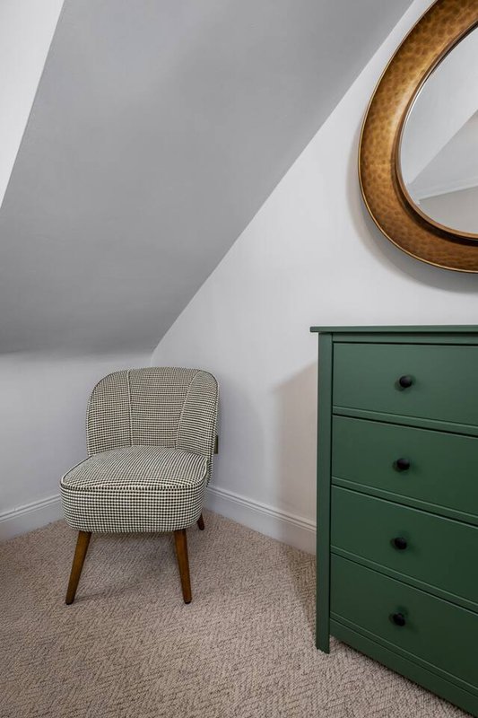 Attic bedroom with cream upholstered chair, green dresser, wooden mirror frame