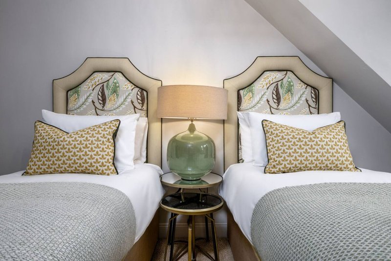 Twin bedroom with matching upholstered headboards, white bedding, patterned cushions and central side table