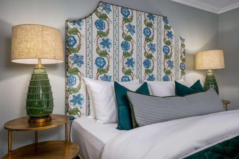 Bedroom with double bed, patterned headboard, decorative pillows, and brass table lamps