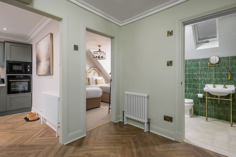 Open-plan hallway with herringbone wood flooring, pale green walls, and doorways to bedroom, kitchen, and bathroom