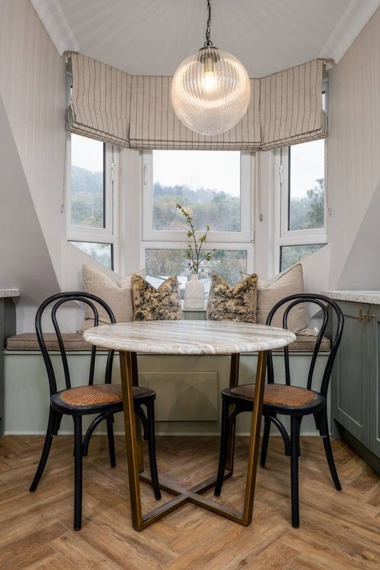 Bright dining nook with round marble table, black chairs, pendant light and bay windows overlooking countryside
