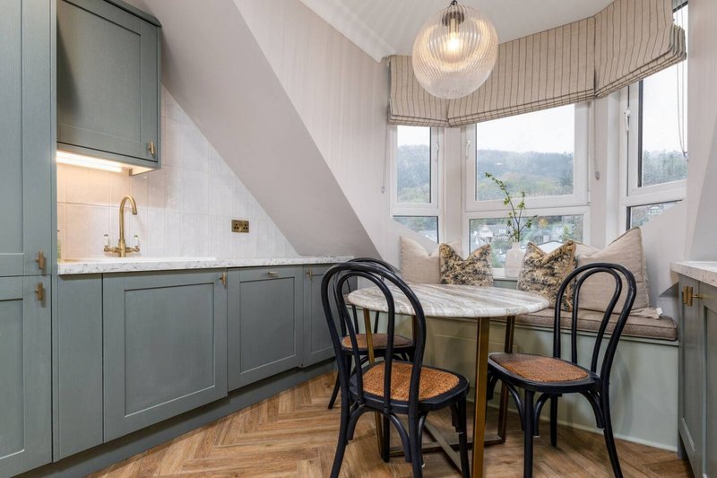 Bright attic kitchen with grey cabinetry, dining table, two black chairs and mountain views