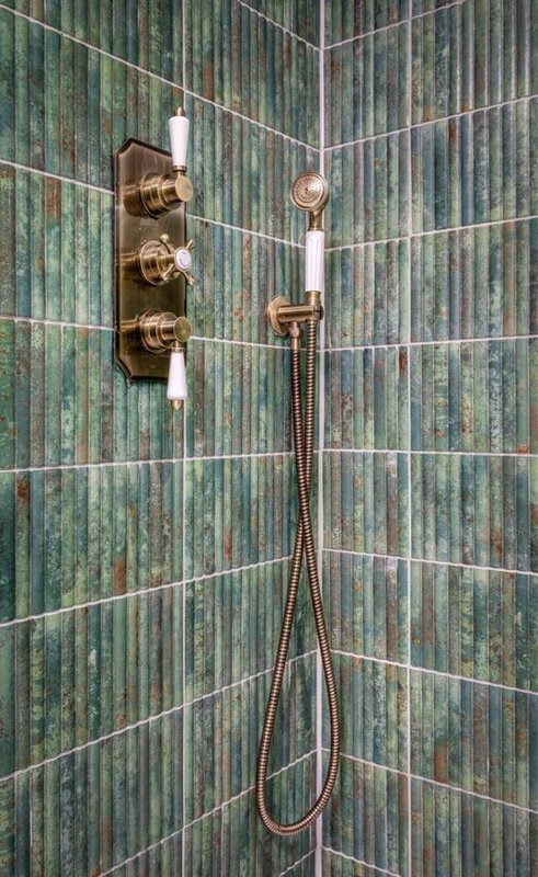 Bathroom shower with green tile walls, brass fixtures and handheld showerhead