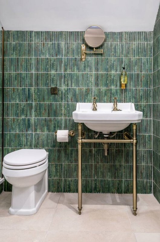 Modern bathroom with green tile wall, pedestal sink, toilet, and round mirror