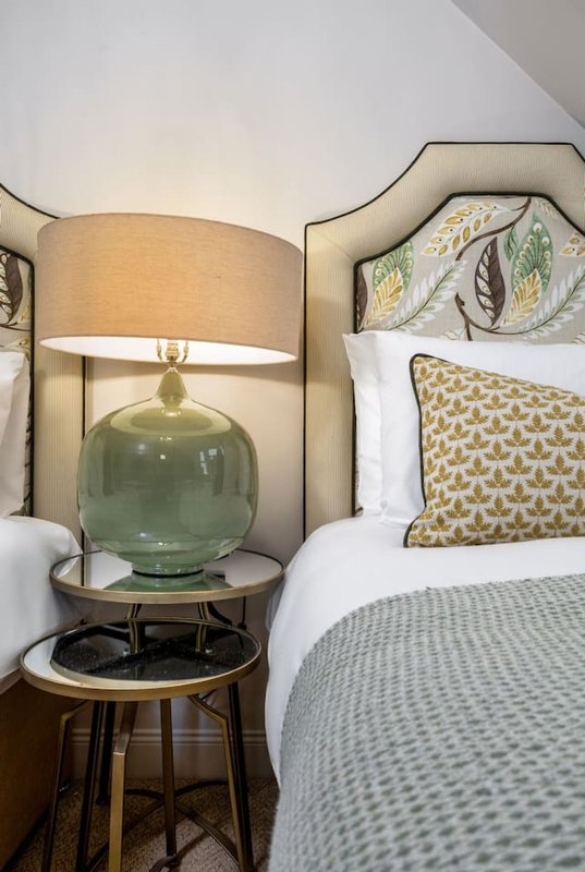 Modern bedroom with upholstered headboard, green glass table lamp, and patterned cushions on bed