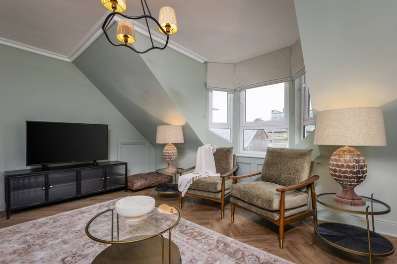 Bright attic living room with sloped ceiling, two armchairs, TV stand, and large windows