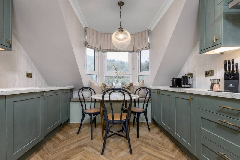 Modern galley kitchen with green cabinetry, white countertops, dining table and chairs, pendant lighting