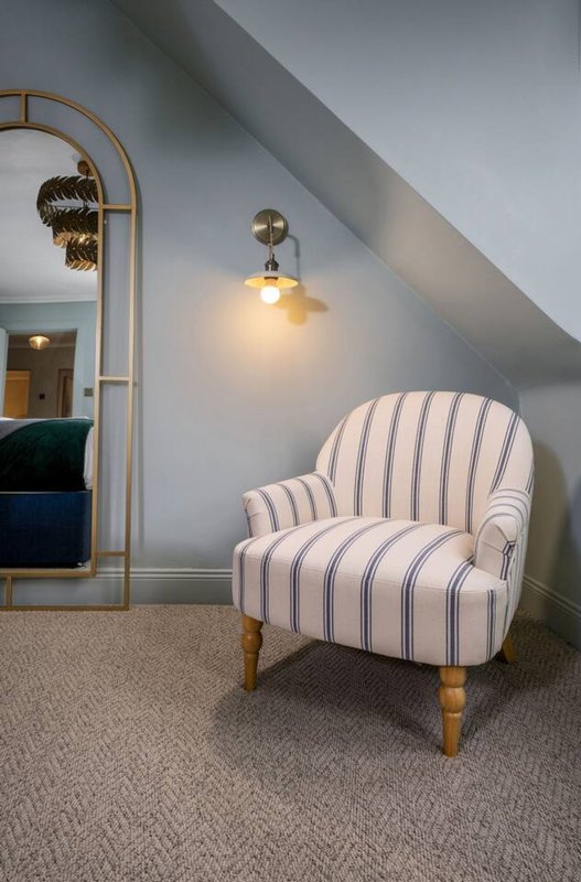 Attic bedroom with striped accent chair, brass floor lamp, and pendant light