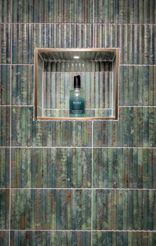 Recessed wall niche in green tiled bathroom wall with single dark bottle displayed