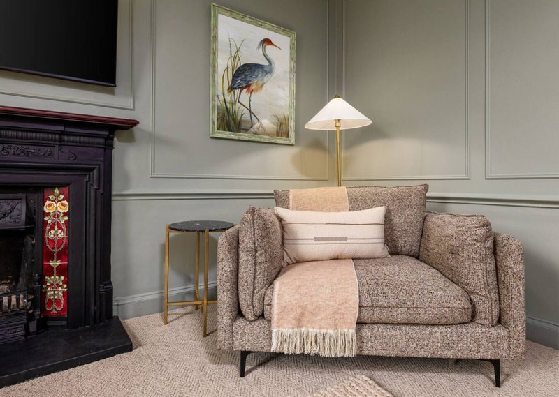 Living room with beige upholstered sofa, fireplace, framed bird artwork, and table lamp