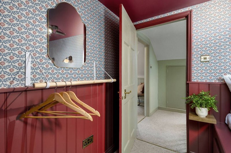 Hallway with patterned wallpaper, burgundy paneling, wooden hangers and mirror