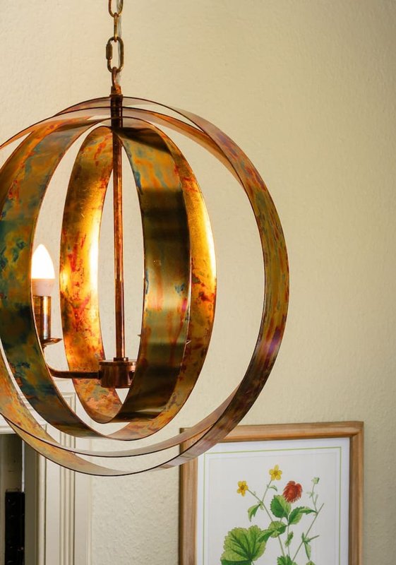 Spherical copper pendant light fixture hanging from chain with framed botanical artwork below