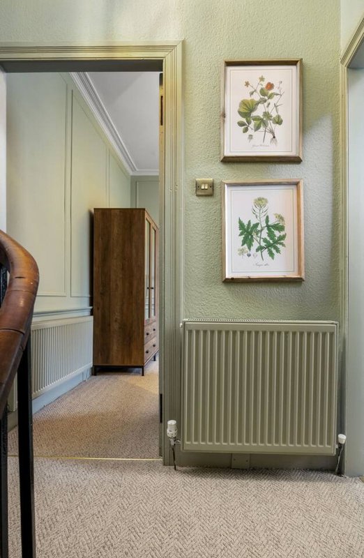 Bedroom with open doorway, framed botanical prints, radiator and carpeted floor
