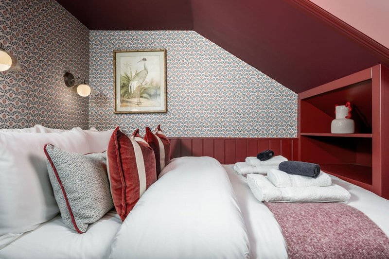Attic bedroom with twin beds, patterned wallpaper, red accents and framed artwork