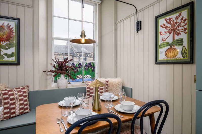 Dining area with wooden table, bentwood chairs, window seat with cushions and garden view