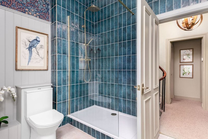 Modern bathroom with blue tiled shower enclosure, white toilet, and access to hallway