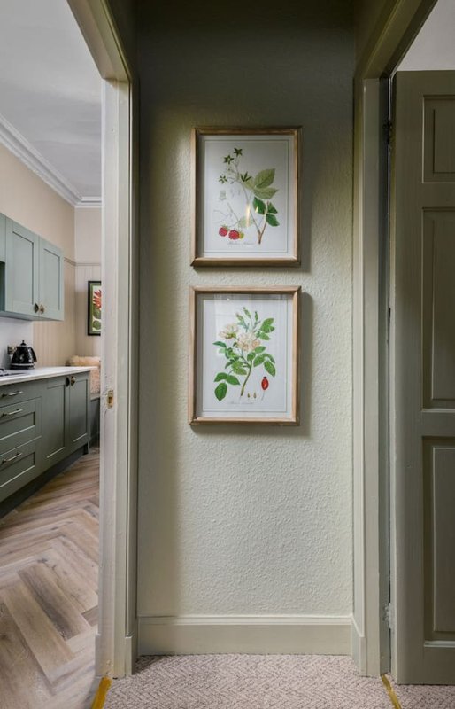Hallway with framed botanical prints on wall, kitchen visible through doorway