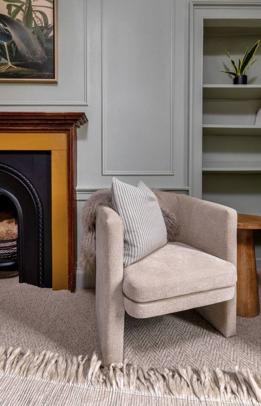 Beige upholstered armchair with striped cushion near fireplace and built-in shelving