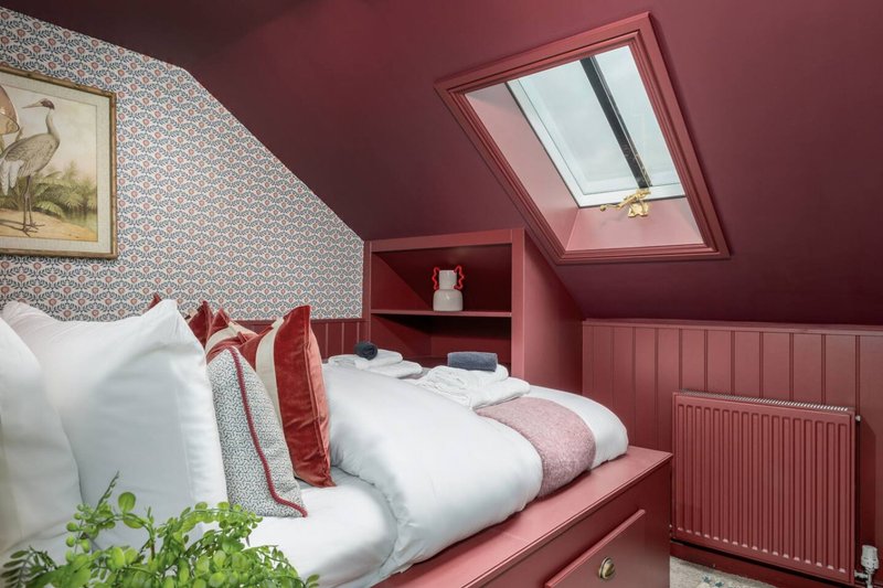 Attic bedroom with burgundy walls, skylight, single bed with white bedding and red cushions
