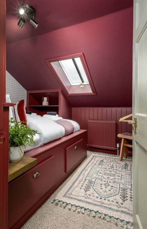 Compact bedroom with burgundy walls, built-in bed with white bedding, skylight window and wooden furnishings
