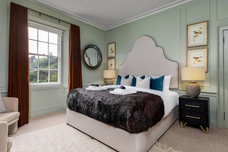 Bedroom with upholstered bed, dark fur throw, blue pillows, pale green walls and window