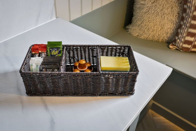 Woven basket organizer on white countertop containing tea boxes and accessories