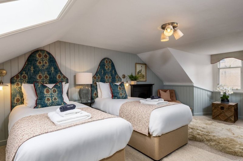 Attic bedroom with two single beds, teal headboards, white bedding and sloped ceiling