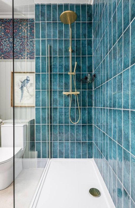 Modern bathroom with teal tile shower, gold fixtures, white walk-in tray and toilet