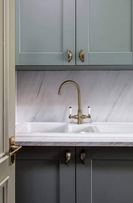 Modern kitchen sink with marble backsplash, brass faucet, and gray cabinetry