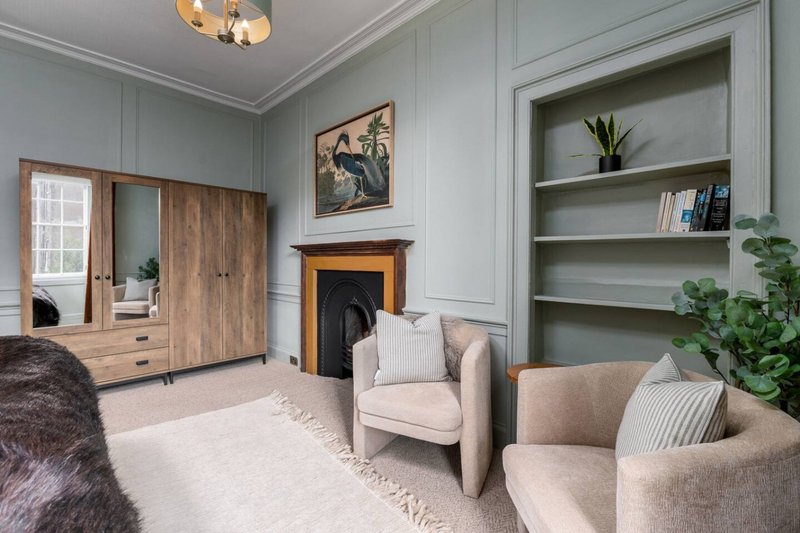 Contemporary bedroom with cream armchairs, fireplace, wooden wardrobe and built-in shelving