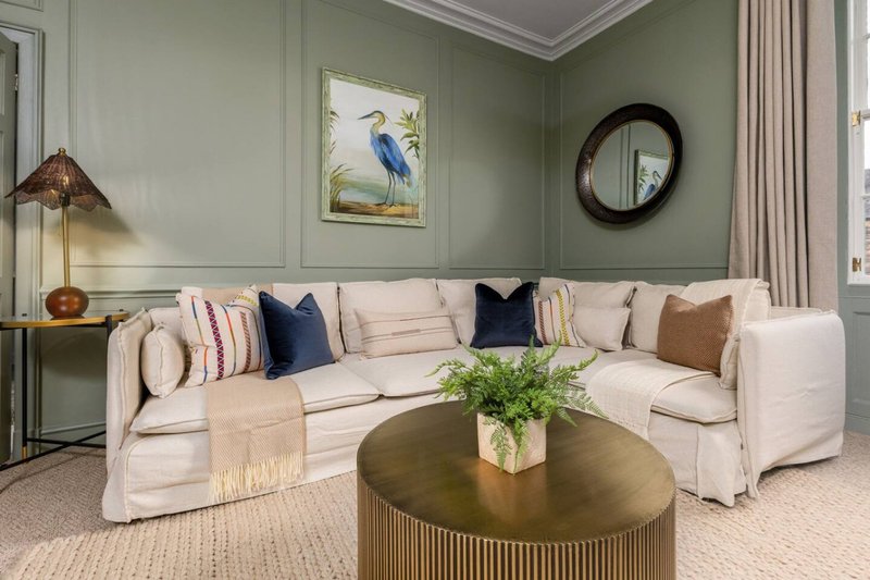 Elegant living room with cream sectional sofa, brass coffee table, green walls, and decorative artwork