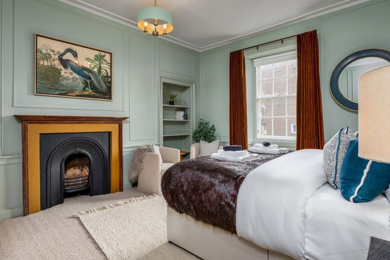 Bedroom with fireplace, double bed, window with red curtains, and pale blue walls
