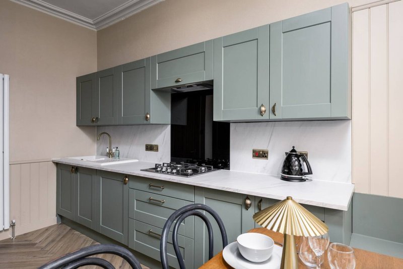 Modern kitchen with sage-green cabinetry, white countertop, gas hob and integrated appliances