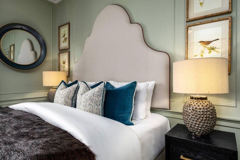 Bedroom with upholstered headboard, layered pillows, bedside lamp and framed wall art