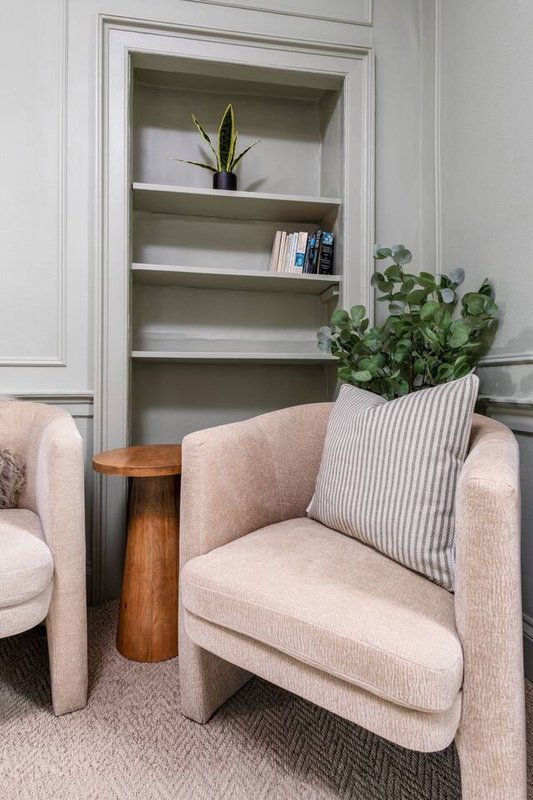Cream upholstered armchair with striped cushion, wooden side table, and built-in shelving with plants and books