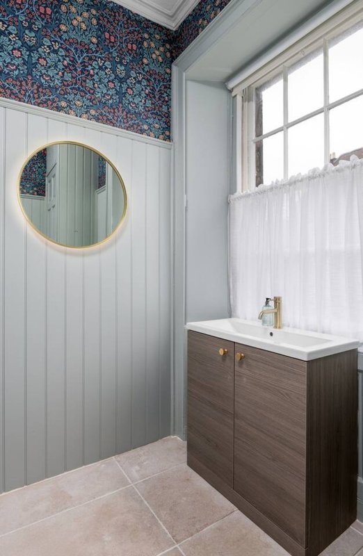 Modern bathroom with round mirror, wooden vanity, white subway tiles and patterned wallpaper