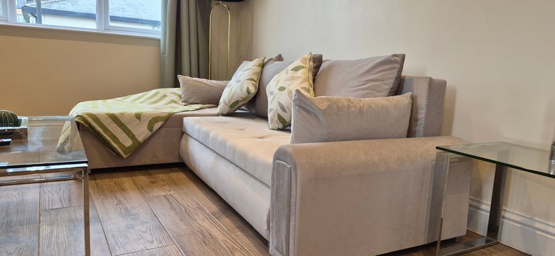 Living room with gray sectional sofa, decorative pillows, wooden floor, and window with curtains
