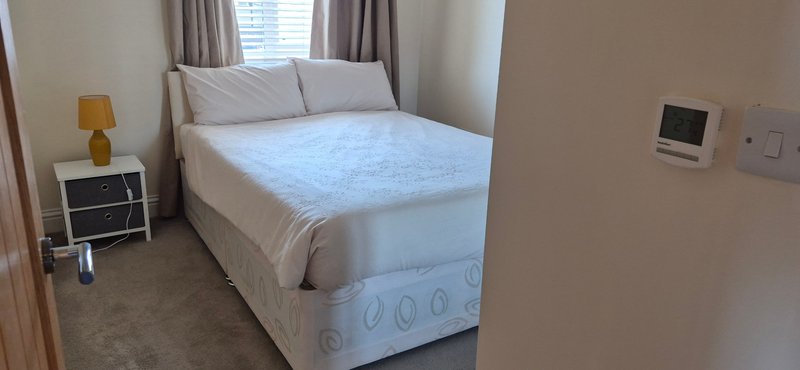 Bedroom with double bed, bedside lamp, small nightstand, curtains and wall thermostat
