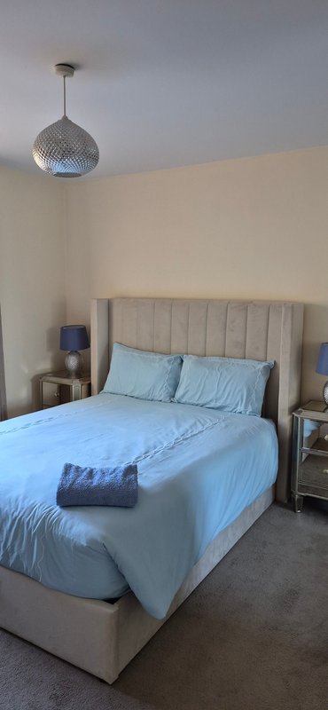 Bedroom with blue bedding, upholstered headboard, pendant light, and nightstands