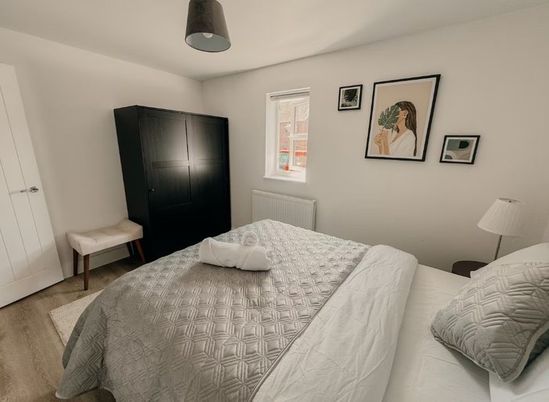 Bright bedroom with double bed, black wardrobe, window, wall art and bedside lamp