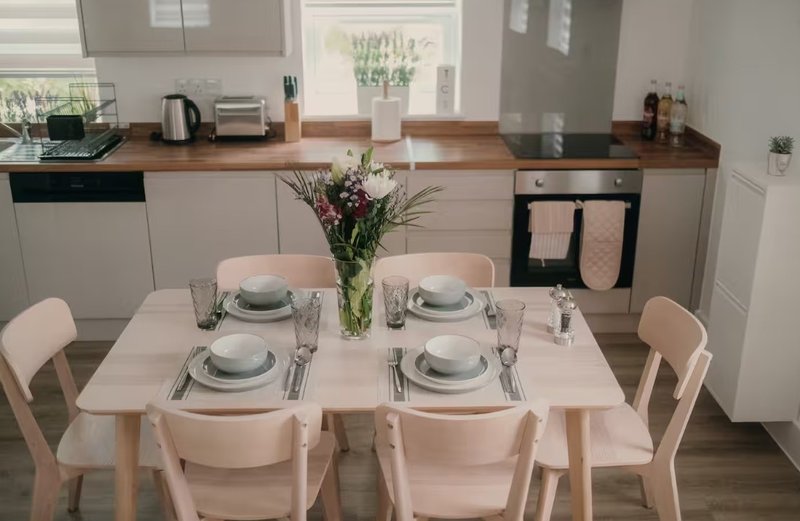 Modern kitchen-diner with white cabinetry, wooden dining table set for four, and integrated appliances