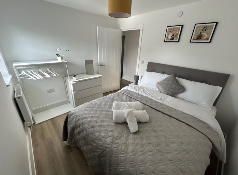 Bright bedroom with double bed, grey headboard, white crib, and wooden flooring