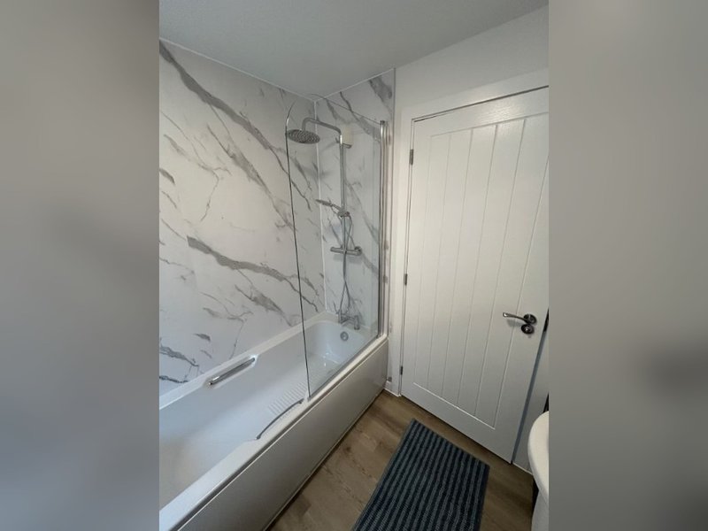Modern bathroom with marble-effect shower enclosure, white panelled door and wooden floor