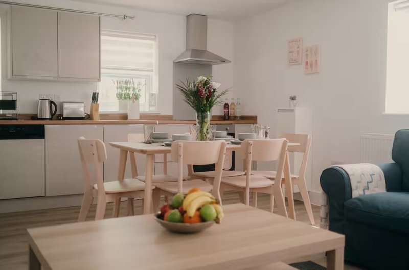 Open-plan kitchen and dining area with wooden table, chairs, and fresh flowers in vase